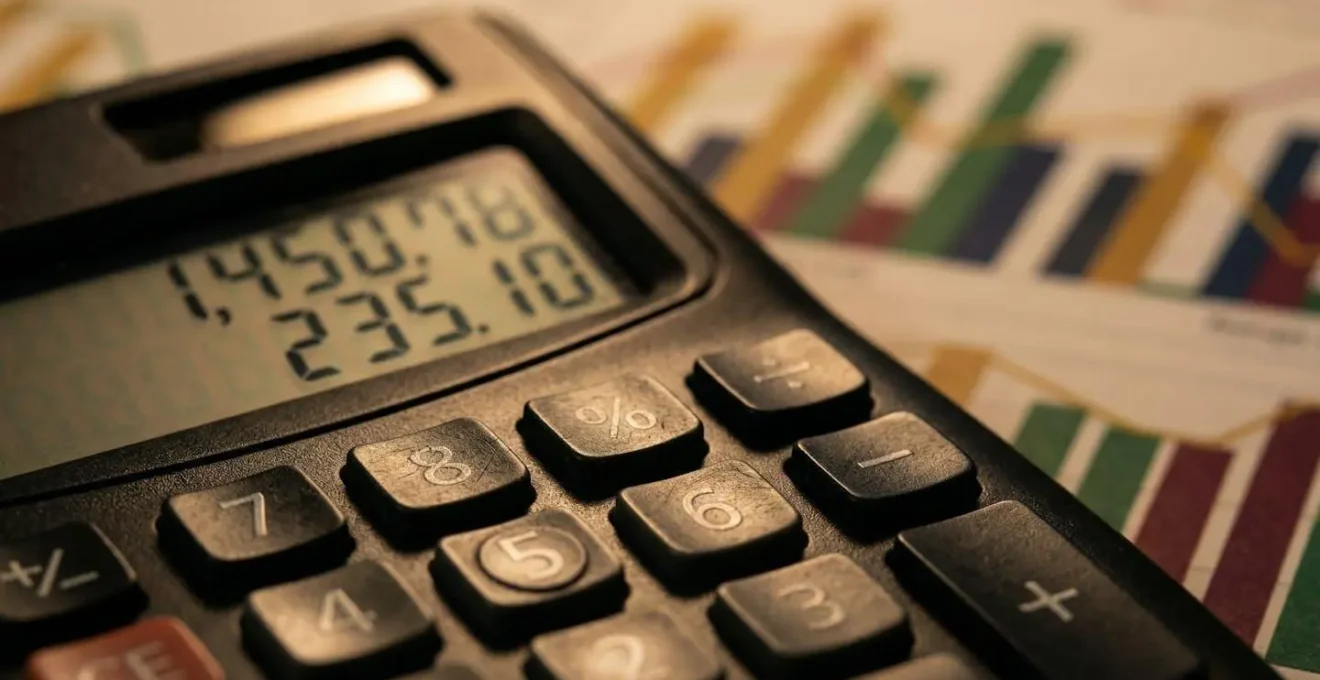 Bureau avec calculatrice professionnelle et graphiques financiers en arrière-plan flou